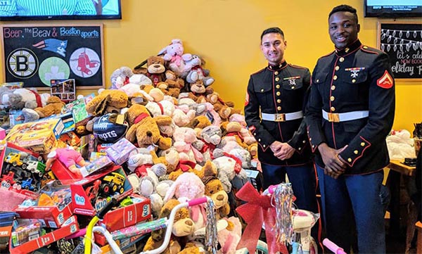 two Marines from Toys for Tots standing next to a large pile of teddy bears and other toys